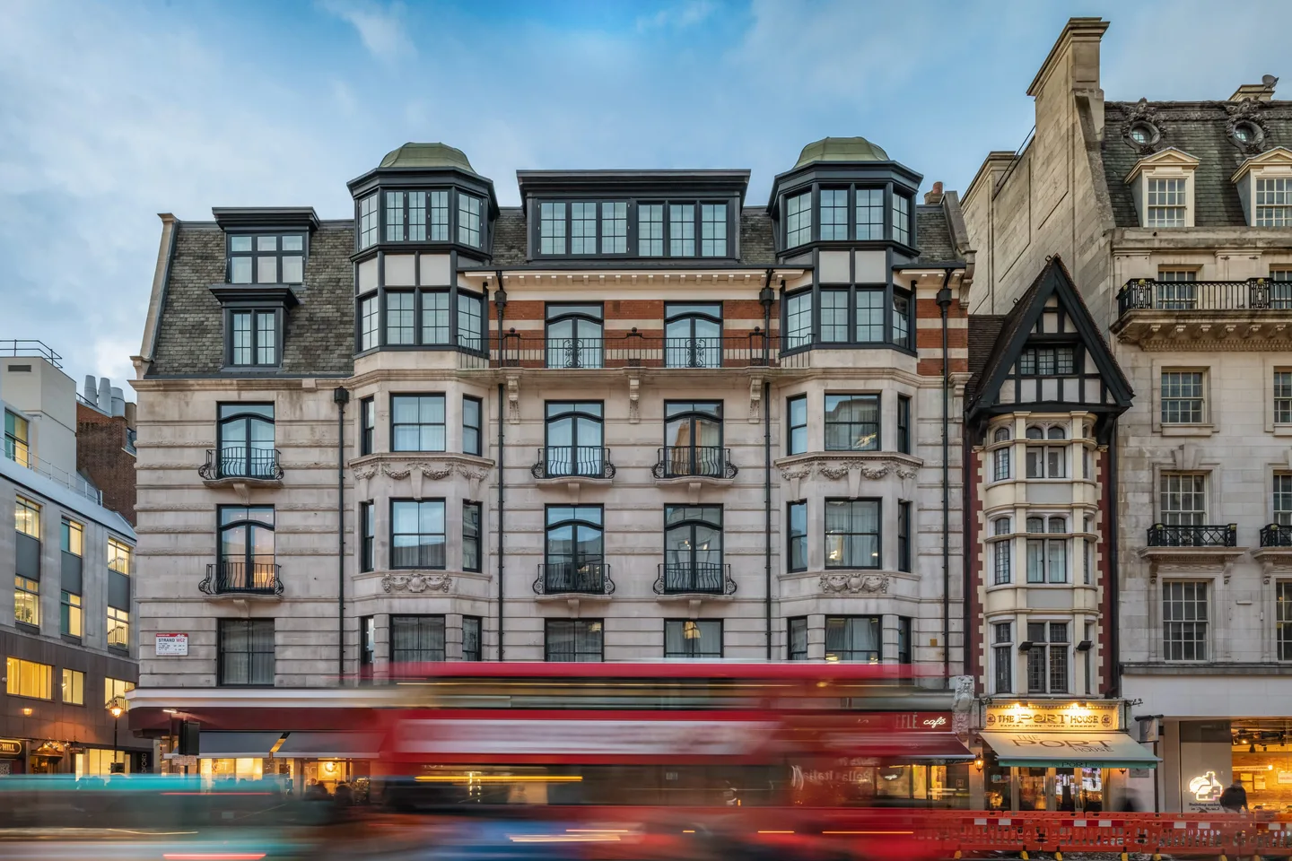 The exterior of The Resident Covent Garden above street-level shops, with a red London bus passing in front.