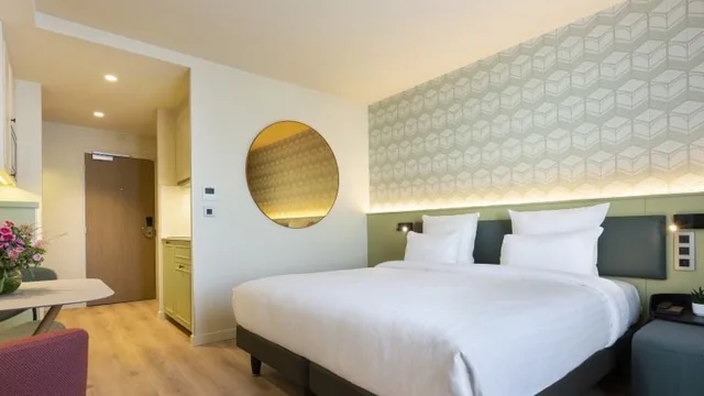Double bed, round wall mirror and kitchenette entrance in a Studio at Citadines Les Halles Paris.